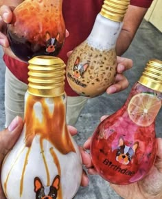 three people are holding different colored bottles with designs on them and one has an orange slice