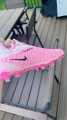 a person holding a pink nike shoe on top of a wooden deck next to a picnic table