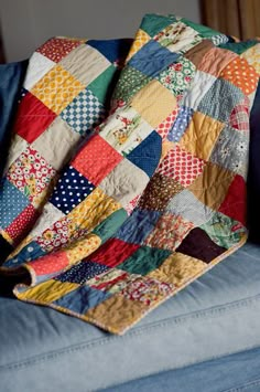 a blue couch with a multicolored patchwork quilt on it's back