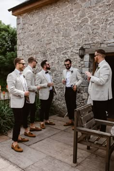 a group of men standing next to each other in front of a stone building wearing suits and ties