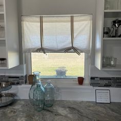 two vases are sitting on the counter in front of a window with blind shades