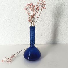 a blue vase filled with pink flowers on top of a white table next to a wall