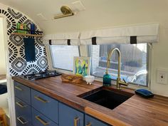 a kitchen with blue cabinets and wooden counter tops in a mobile home that has an art work on the window sill