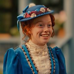 a woman wearing a blue hat with flowers on it's brim smiles at the camera