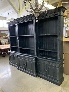 an old black china cabinet in the middle of a room with boxes and chandelier