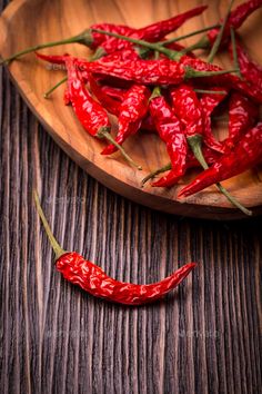 red chili peppers on a wooden plate with green stems in the background - stock photo - images