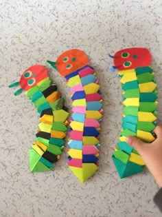 a child's hand is reaching for the caterpillars made out of construction paper