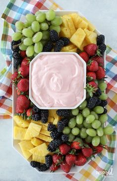 a platter with fruit, cheese and dip in it on a checkered table cloth