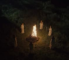 people standing around a campfire in the dark with long white dresses on and holding torches