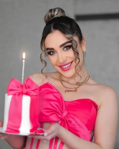 a woman in a pink dress holding a cake with a lit candle on the top