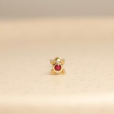 a gold ring with a red stone in the center on a white surface, close up