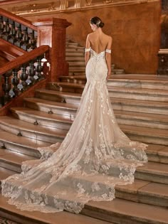 a woman in a wedding dress is standing on some stairs with her back to the camera