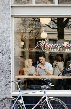 two people sitting at a table in front of a coffee shop with a bicycle parked next to it