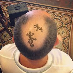 the back of a man's head with an intricate lizard tattoo on his forehead