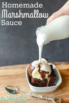 homemade marshmallow sauce being poured over a chocolate cake in a white dish on a wooden table