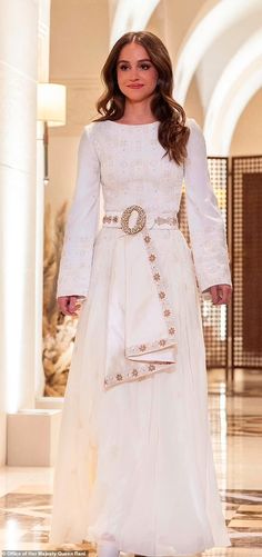 a woman in a white dress walking down a hall with her hand on her hip