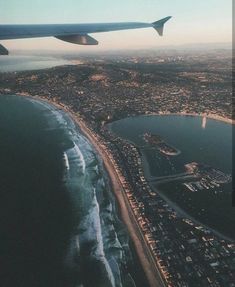 an airplane wing flying over a large body of water next to the ocean and land