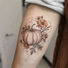 a woman's arm with a pumpkin and flowers tattoo on the left side of her arm