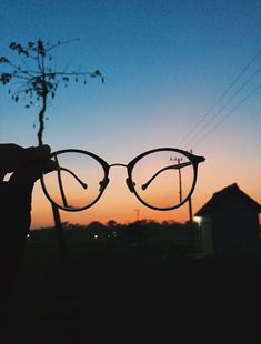 a person holding up some glasses in front of the sun at dusk or dawn,