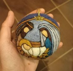 a hand holding a small round ornament with a painting on it