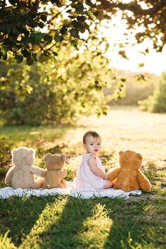 a baby sitting in the grass with three teddy bears next to her on a blanket