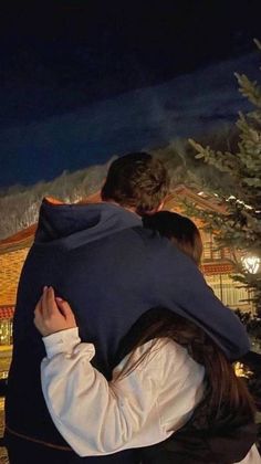 a man and woman hugging each other in front of a building with lights on it