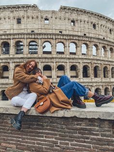 two women are sitting on the wall in front of an ancient roman collise