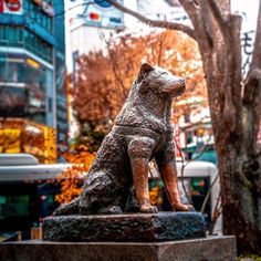 a statue of a dog sitting on top of a cement block next to a tree