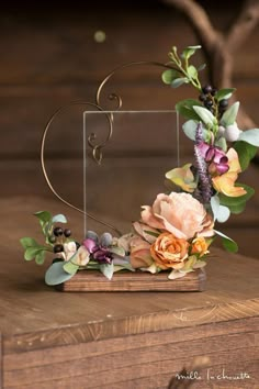 a wooden table topped with a heart shaped vase filled with flowers and greenery on top of it