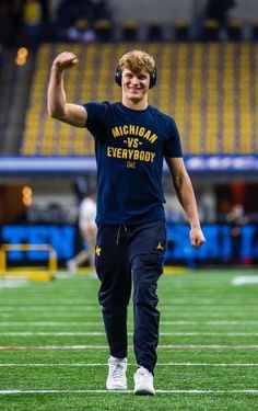 a young man wearing headphones is walking on the field with his arm in the air