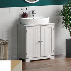 a white sink sitting under a bathroom mirror next to a potted plant and green wall