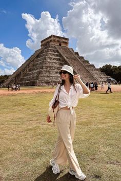 a woman is standing in front of an ancient pyramid with her hand on her head