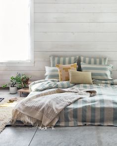 a bed with blue and white striped comforter on top of it next to a window