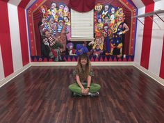 a woman is sitting on the floor in front of clowns painted on the walls