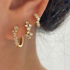 a close up of a person's ear wearing gold earrings with small white stones