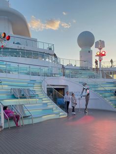 people are standing on the deck of a cruise ship at sunset with stairs leading up to them