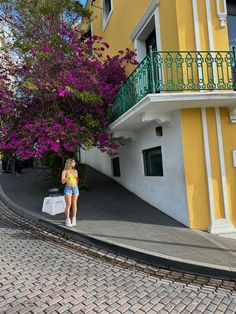 a woman standing on the side of a road next to a yellow and white building