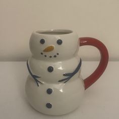 a ceramic snowman mug sitting on top of a white table next to a red handle