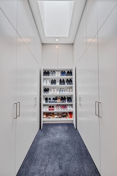 a walk in closet filled with lots of white cupboards and shoes next to a blue carpet