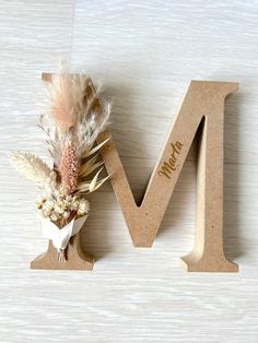 the letter m is made out of wood and has feathers on it, along with dried flowers