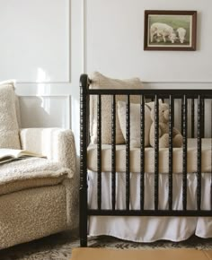 a baby's crib in the corner of a room with a chair and pictures on the wall