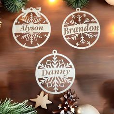 three personalized christmas ornament hanging from a wooden wall next to pine cones