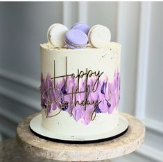 a birthday cake with purple and white frosting on a wooden stand in front of a wall