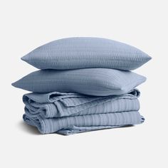 three pillows stacked on top of each other in light blue linens, one folded and the other rolled up