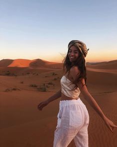 a woman standing in the desert with her arms spread out and smiling at the camera