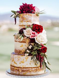 a three tiered cake with flowers and greenery on the top is sitting on a table