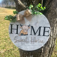 a home sign hanging from the side of a tree in front of a grassy field