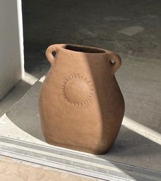 a brown vase sitting on the ground in front of a door way with an open window behind it