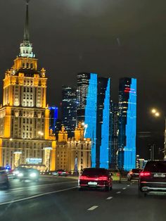 cars are driving down the street in front of tall buildings at night with bright lights