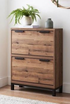 a wooden dresser with two drawers next to a potted plant on top of it